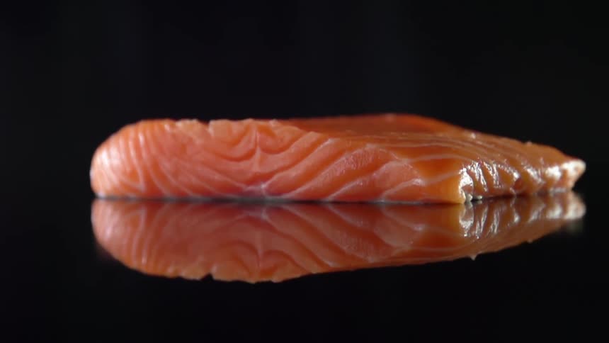 Raw salmon steak being placed on a reflective counter