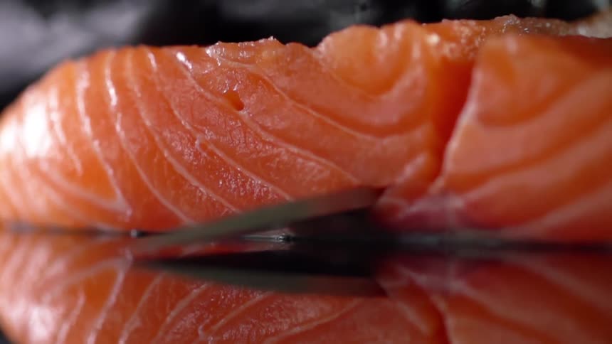 Cook with black gloves cuts fish for sushi