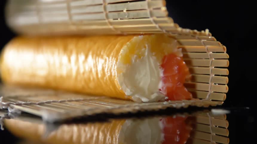 A person with black gloves unwrapping sushi that is wrapped in bamboo