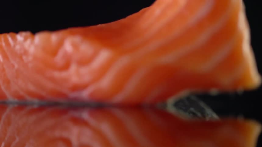 A fillet of fish slowly uncurls while lying on a reflective black surface