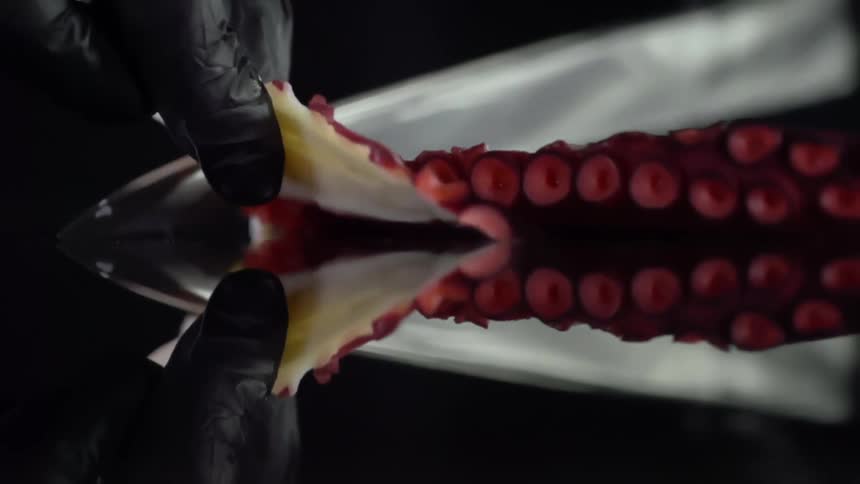 A gloved chef cuts thin slices of octopus with a large knife