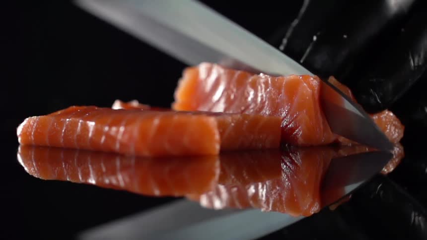 A cook with black gloves cuts fish for sushi in studio