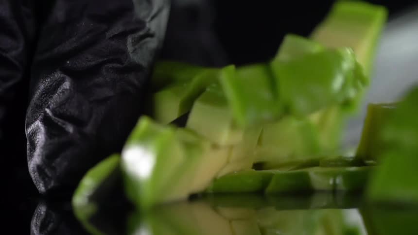 A person with black gloves chopping avocados with a knife