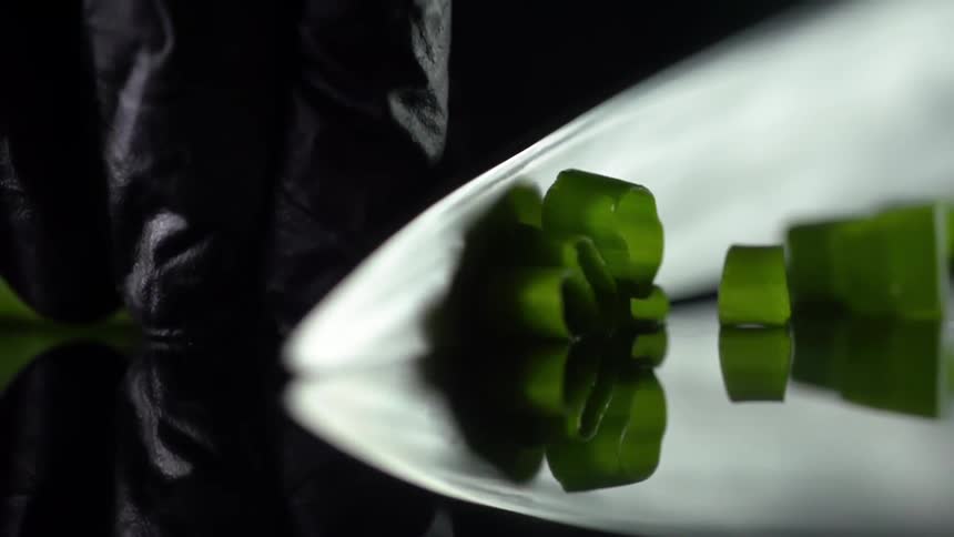 Fingers wearing black gloves secure a bundle of chives and a chef knife slices through the bunch