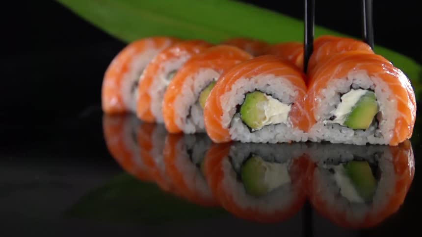A sushi roll is being taken by chopsticks in studio