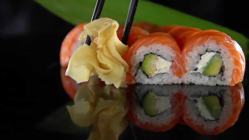 Chef places garnish with chopsticks near to salmon sushi