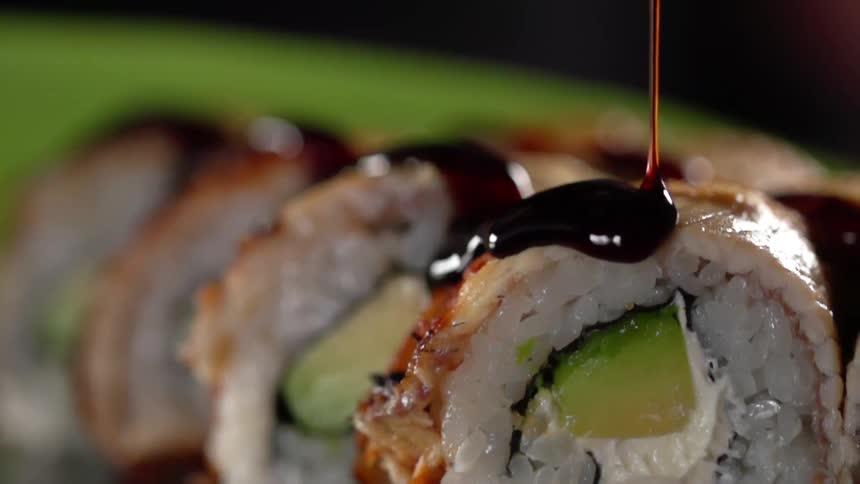 Brown sauce pouring on top of sushi rolls