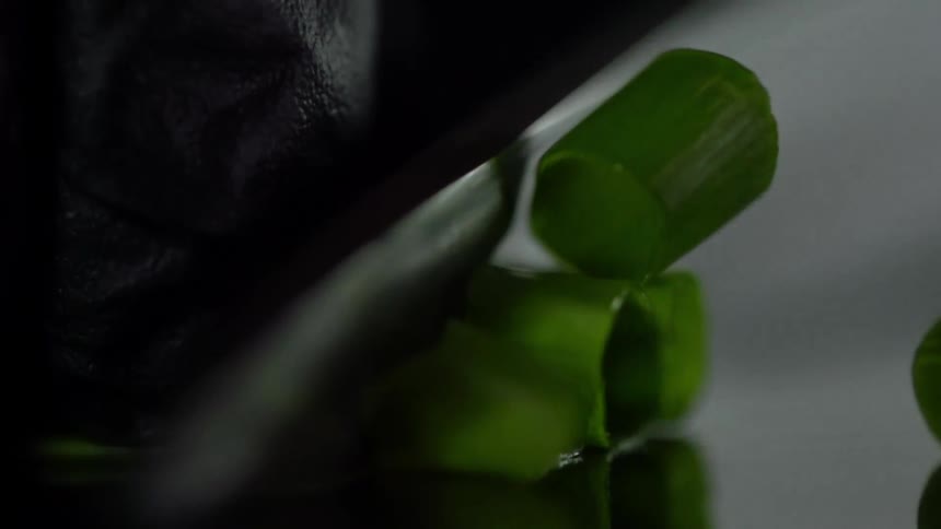Chef wearing black latex gloves slices chives with a sharp kitchen knife