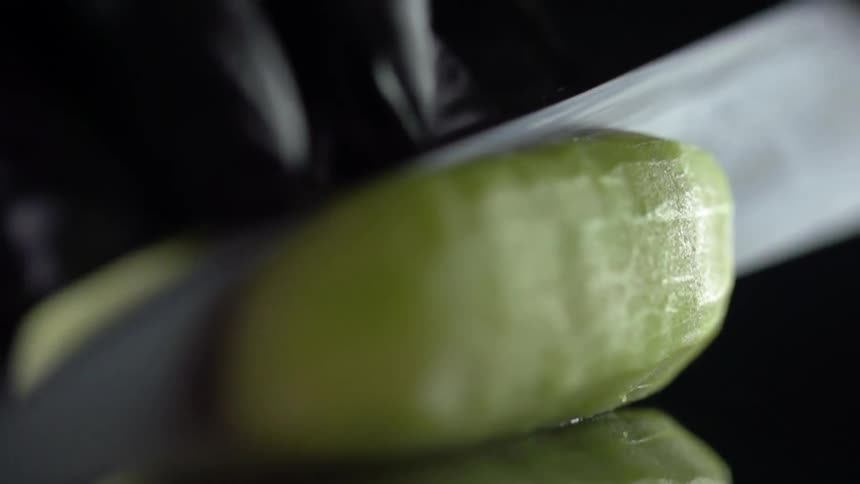Chef wearing black latex gloves slices a cucumber with a sharp kitchen knife