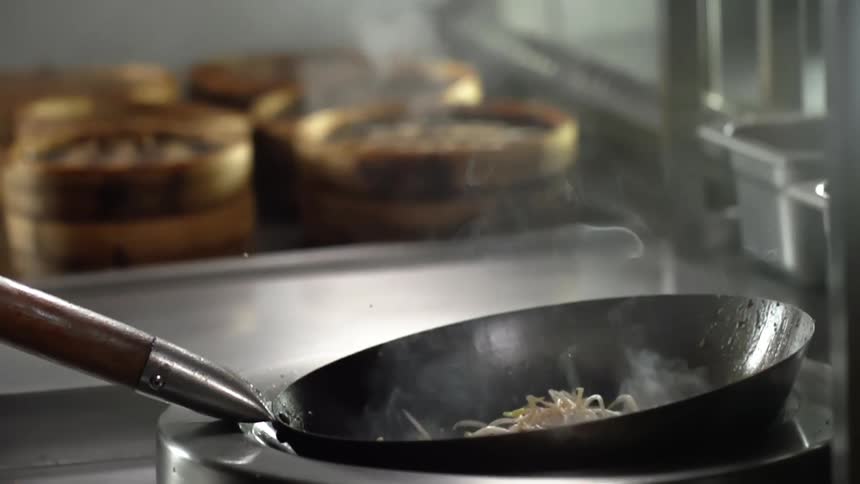 Mung bean sprouts are dropped into a hot wok in a restaurant kitchen