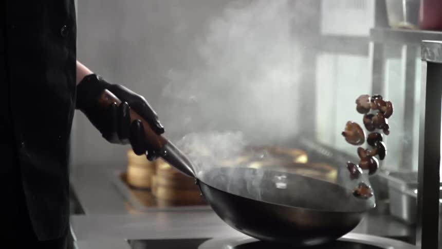 A person cooking and flipping mushrooms in a pan