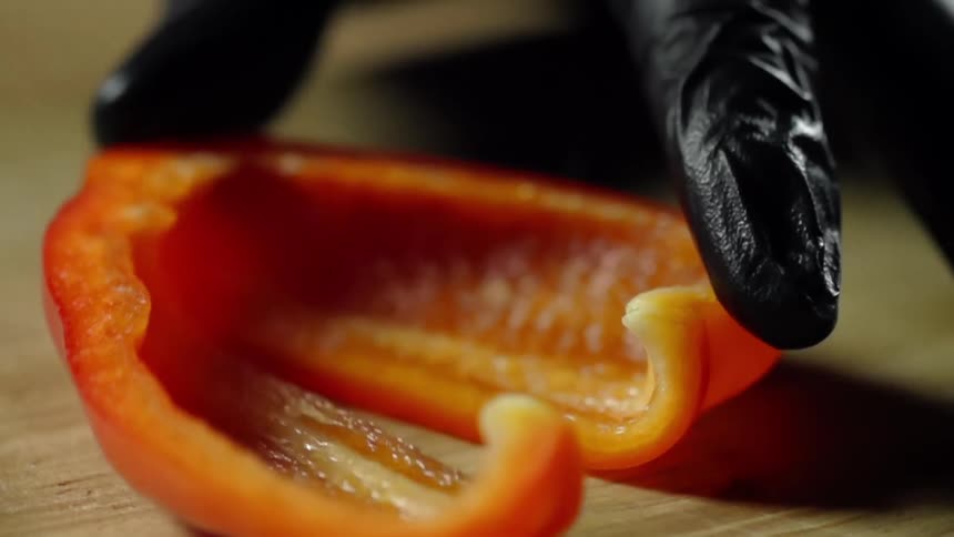 Cook with black gloves cuts a red bell pepper on a cutting board