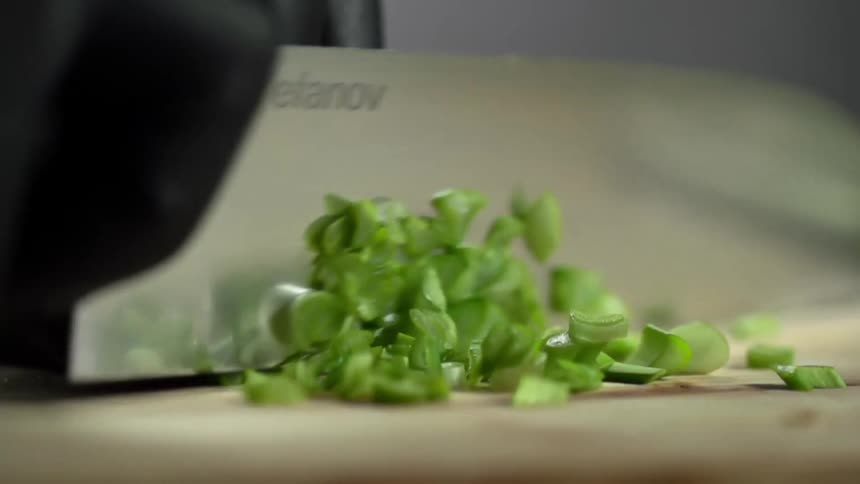 Close up of chef knife chopping the ends of green onions