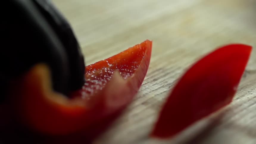 Close up of sharp bladed knife slicing a red bell pepper