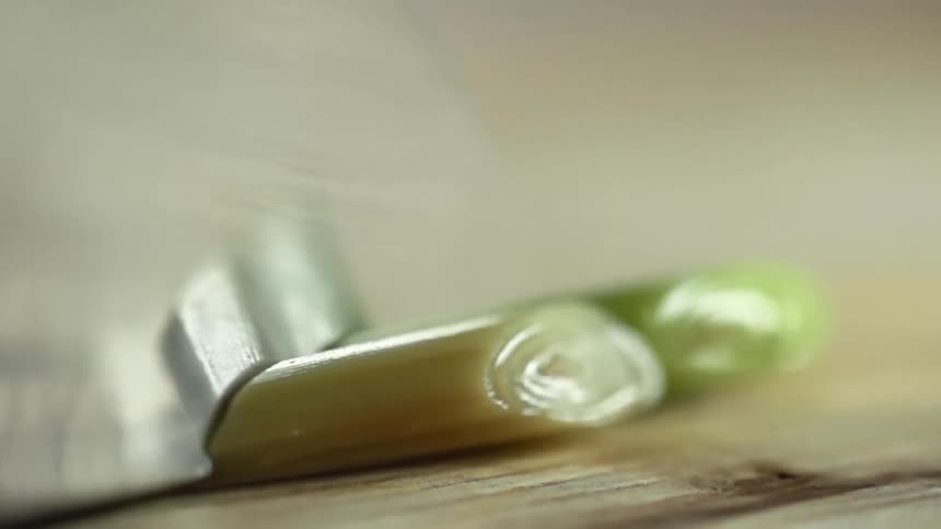 Person in black gloves holds scallion while slicing it