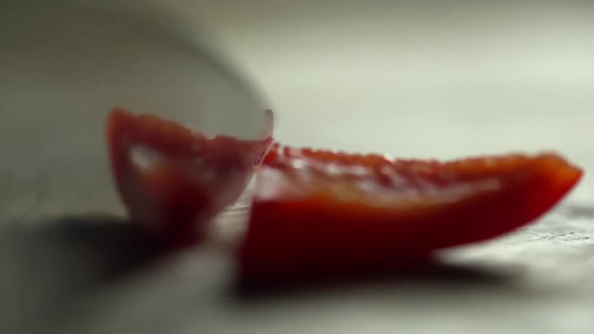 A knife cutting a red bell pepper on the cutting board