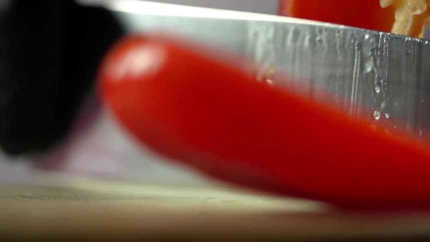 Close up of a red bell pepper being cut by a sharp knife