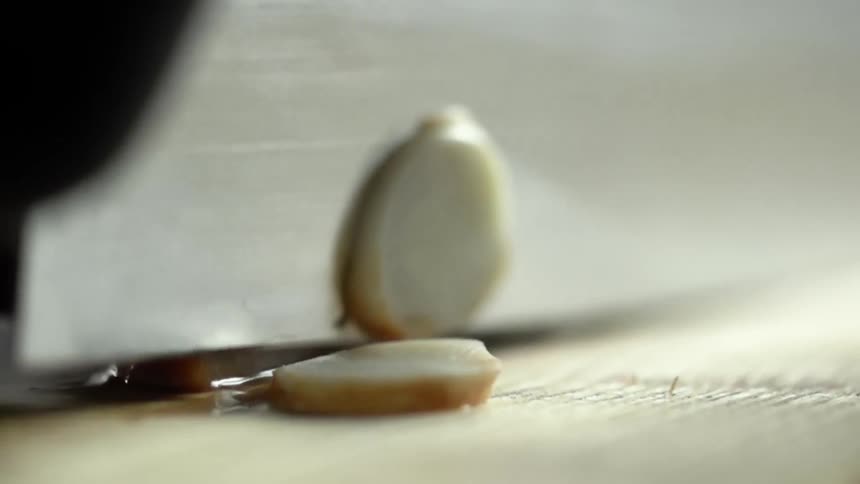 Person wearing black gloves slices garlic with knife