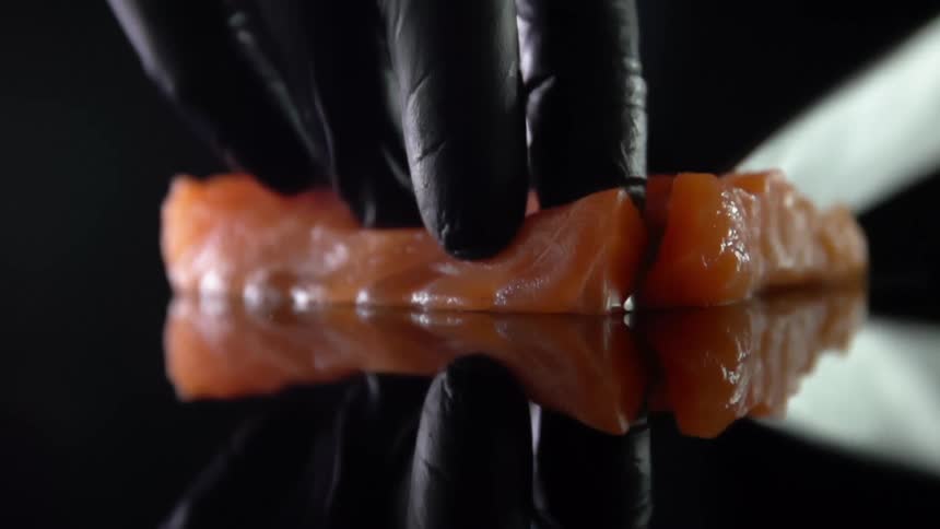 Cook with black gloves cuts fish for sushi in studio
