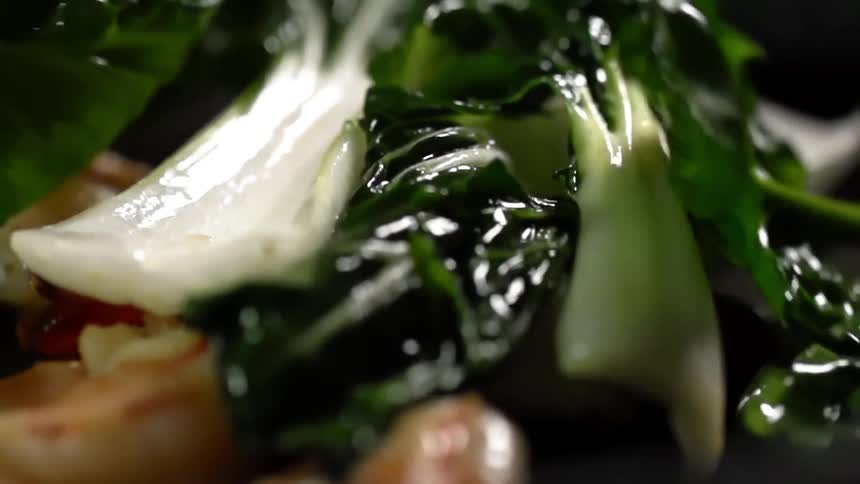 Wet bok choy falling atop oily shrimp in a skillet