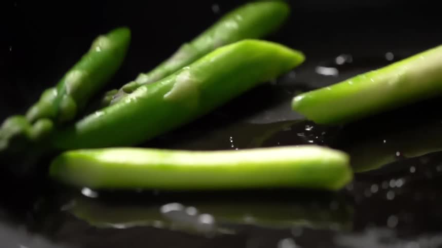 Slices of asparagus falling into and tumbling around an oily skillet