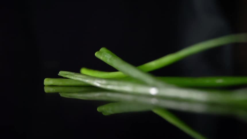Green scallion leaves fall over a reflective surface