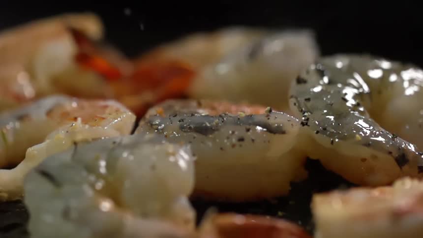 Bits of seasoning fall on a plate of shrimps