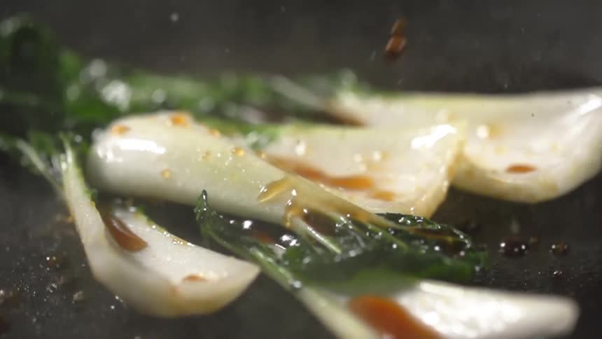 Brown oil drizzles bok choy cooking in a pan