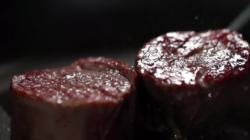 Beef medallions being cooked in a pan with oil sizzling and smoke