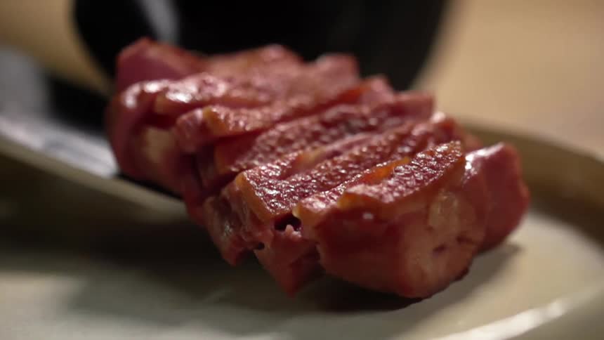Seared and sliced beef is neatly plated from a knife