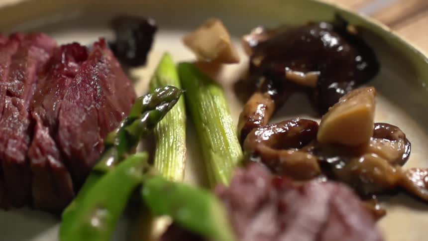 Cooked mushrooms are added to a plate with slices of raw meat and asparagus