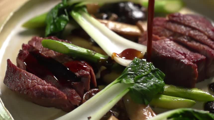 A sauce is drizzled over a plate of steak and bok choy