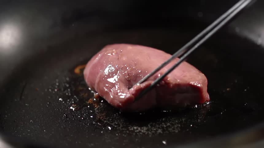 Thin sharp tongs flip a piece of beef over in a hot pan