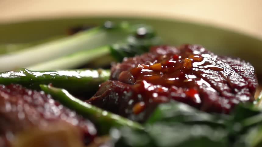 Sauce drips down onto beef steak on a bed of bok choy