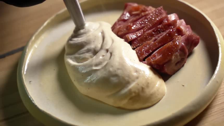 Cream being squeezed from a piping bag onto a plate containing slices of sliced meat