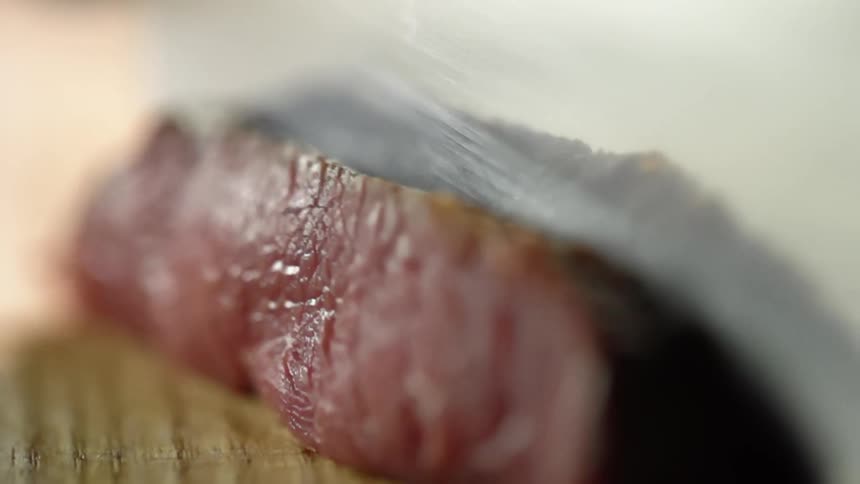 A chef with a sharp knife cuts through a piece of seared beef