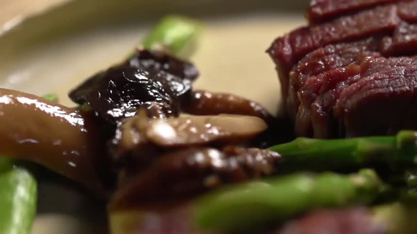 Mushroom are dropped on the plate with sliced beef steak and asparagus