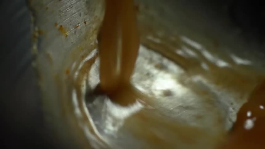 A brown broth pours into a stainless pan