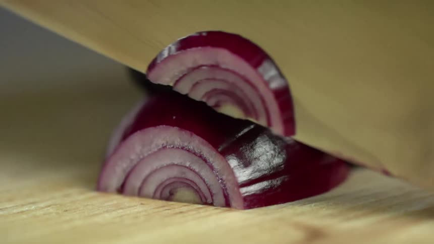 Red spanish onion is being sliced by a knife on a cutting board