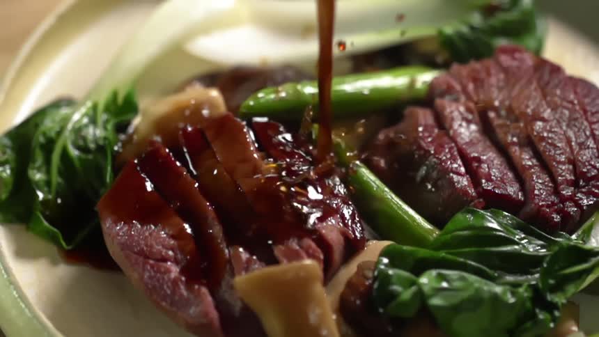 Sauce pouring over steak and bok choy on a plate