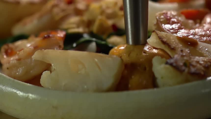 Sauce being squeezed onto a dish of shrimps and cauliflower