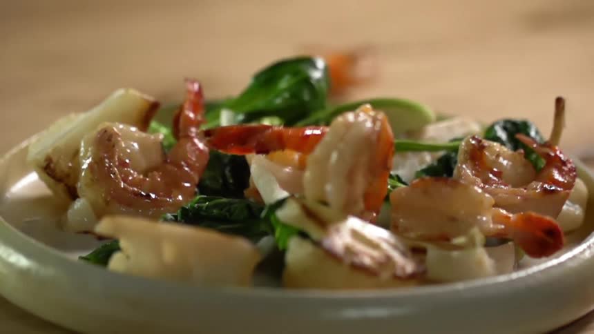 Shrimp dropping onto a plate of cauliflower, bok choy and spinach