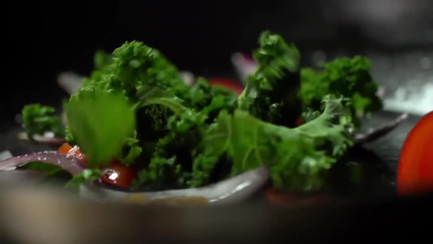 Leafy greens dropping over chopped onions and peppers in a cast iron pan