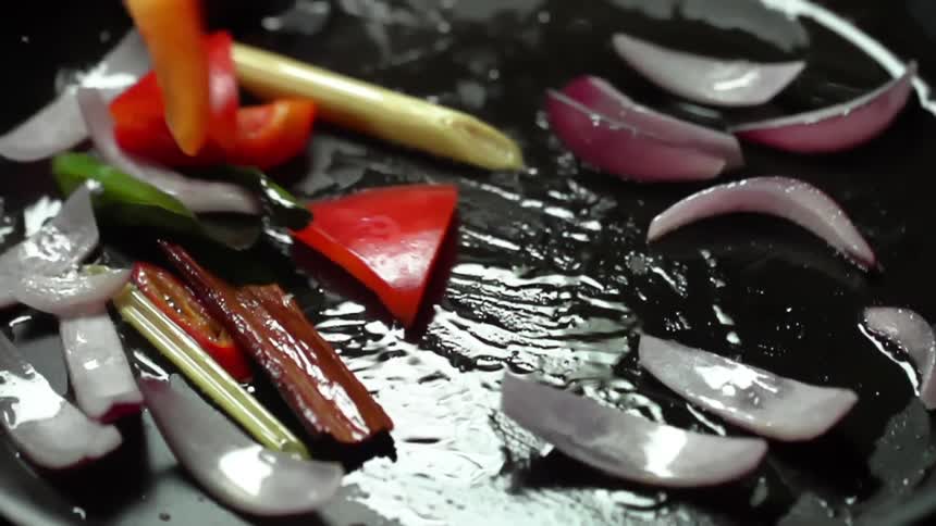 Sliced red peppers are tossed into an oiled pan with onions and fresh herbs
