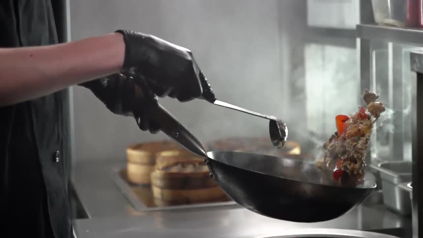 A chef tosses the contents of a steaming hot skillet as they are preparing stirfried food