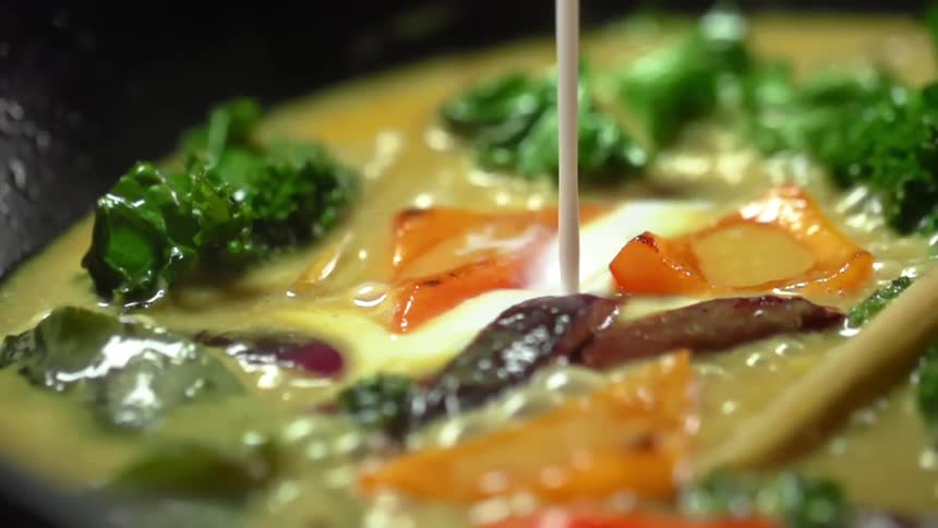 Coconut milk is poured into a simmering pot of curry