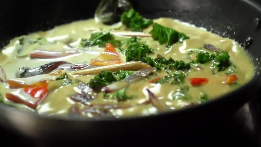 A pan with curry is swirled on a stove top