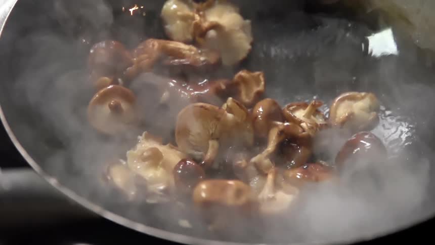 Steam rises as shiitake mushrooms are dropped into a hot wok coated with oil