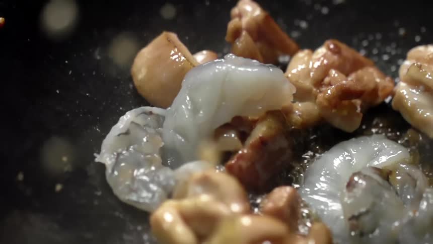 Meat cubes are being roasted while shrimps are being dropped into a black skillet