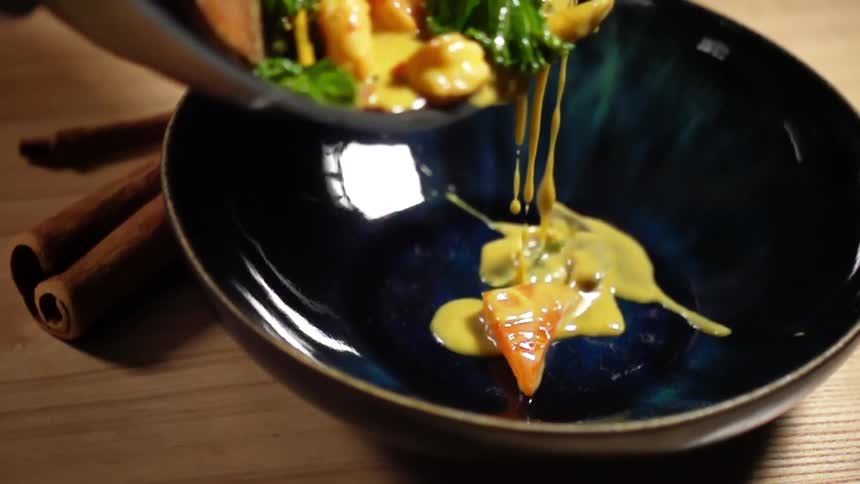 Serving curry shrimps from a pan into a ceramic blue bowl on a wooden table